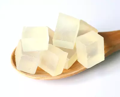 A wooden spoon holding several translucent square jelly cubes on a white background.
