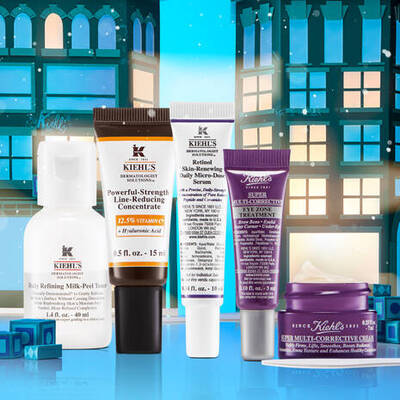 A collection of skincare products from Kiehl's, including a daily refining milk-peel tonic, vitamin C concentrate, retinol cream, eye cream, and a multi-corrective cream, set against a festive backdrop of holiday-themed buildings.