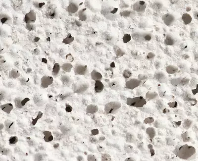 Close-up view of a porous, white-textured surface with small holes and irregular patterns.
