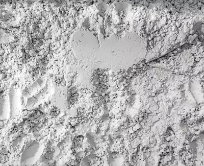 A textured surface of grayish-white powder with a rough appearance, resembling fine dust or mineral particles.