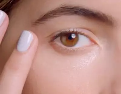 Close-up of a person's eye with brown iris. A finger is gently touching the skin around the eye, showcasing a beauty or skincare routine.