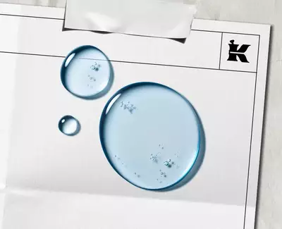 Niebieskie krople płynu symbolizujące α-Bisabolol na białej kartce z czarnym logo Kiehl's w rogu.