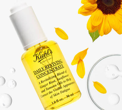Butelka olejku Kiehl's Daily Reviving Concentrate z ingredientami jak imbir i olej słonecznikowy, otoczona płatkami kwiatow.