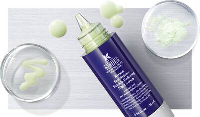Alt text: A tube of Kiehl's wrinkle-reducing serum lies on a metallic surface, accompanied by two small glass dishes containing a green gel and white powder.