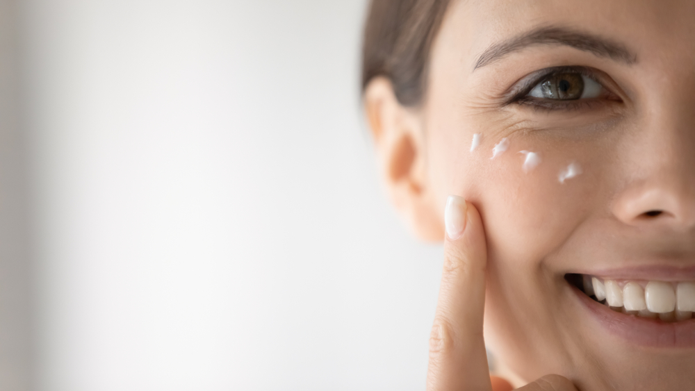 Uśmiechnięta kobieta ma nałożone kremowe serum do twarzy w okolicach oczu