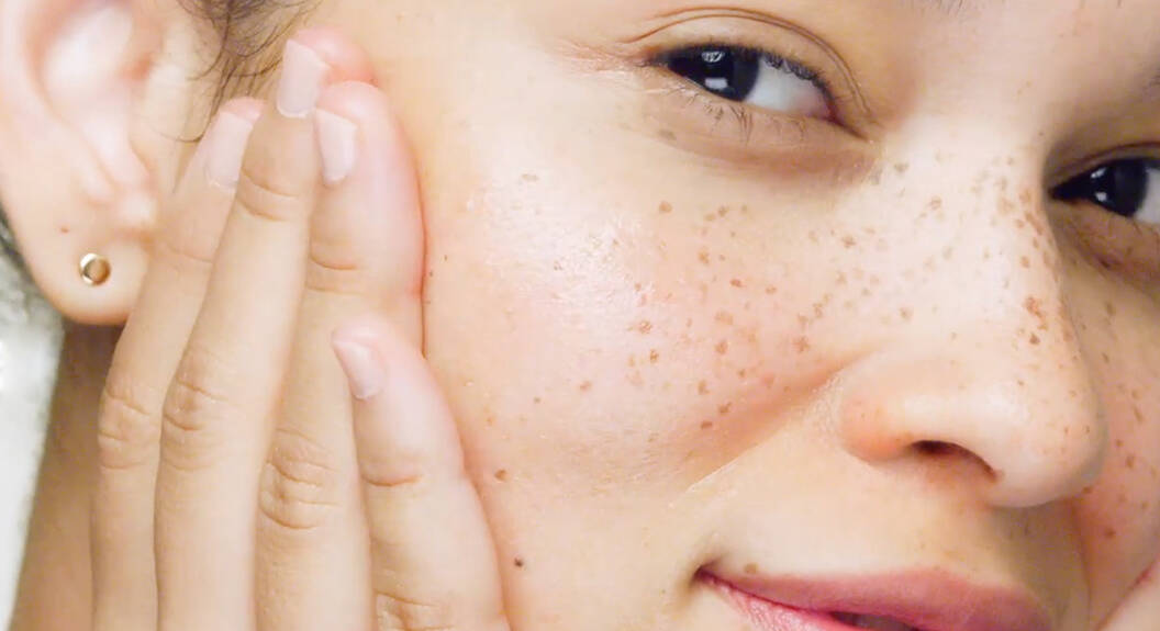 Kobieta patrzy w obiektyw aparatu i lekko się uśmiecha, co uwypukla jej kurze łapki